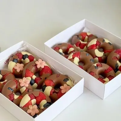 Two boxes of chocolate berry donuts topped with fresh fruit and sugar flowers.