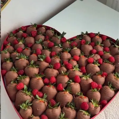 A heart-shaped box packed with chocolate strawberries and fresh raspberries.