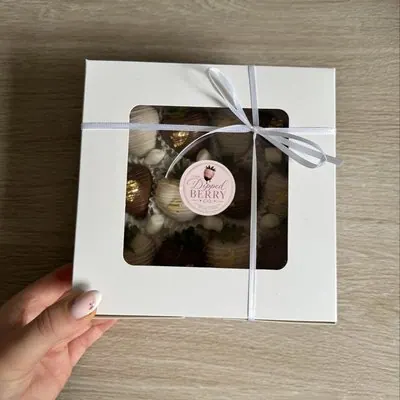 A hand holding a ribbon-tied window gift box of chocolate treats.