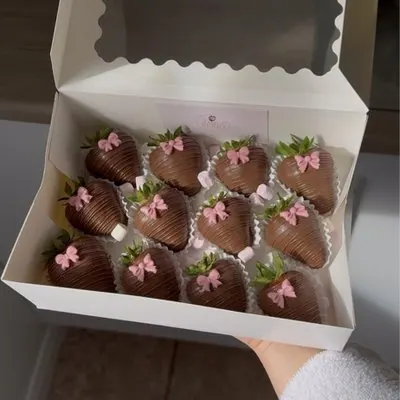 A box of chocolate strawberries, each with a pink bow.